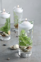 Candles, stones and fern leaves in glass holders with liquid on grey table