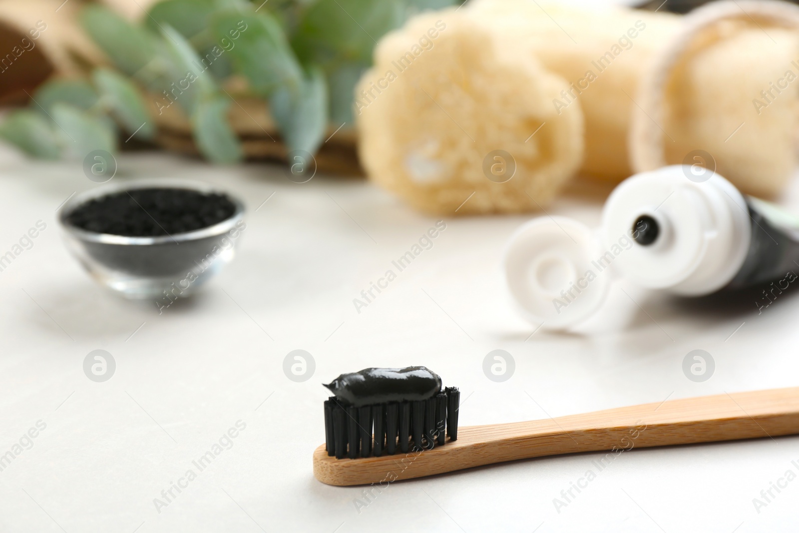 Photo of Bamboo toothbrush with charcoal paste on white table, closeup. Space for text