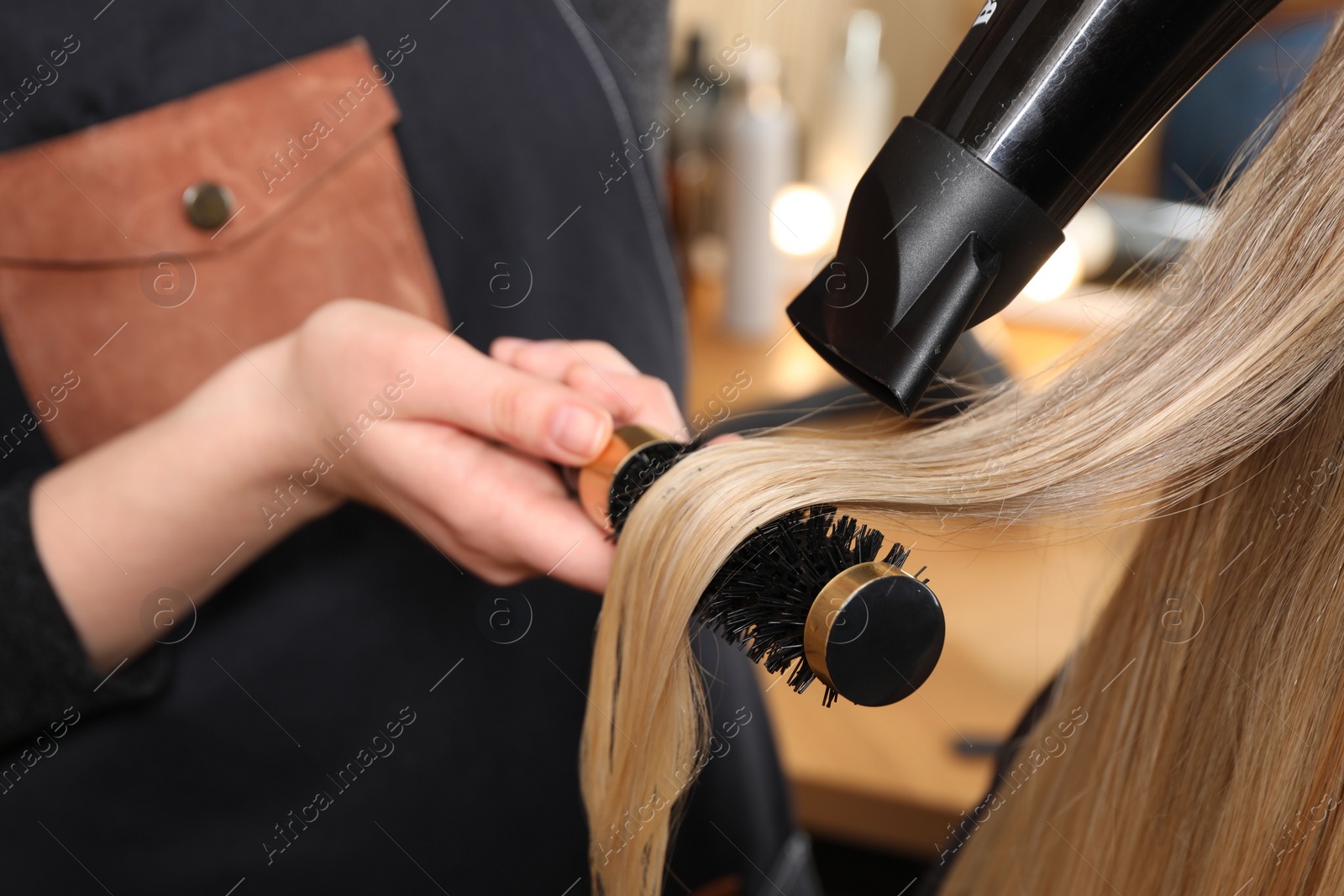 Photo of Hairdresser blow drying client's hair in salon, closeup