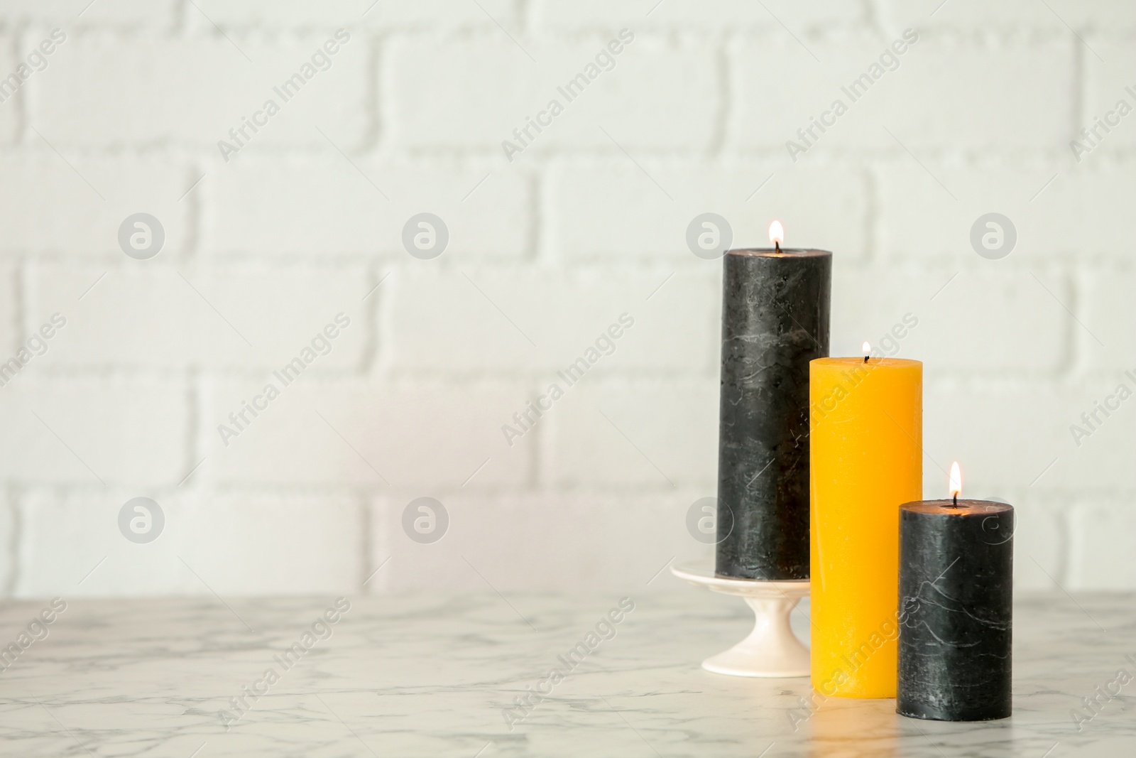 Photo of Different decorative wax candles on table against brick wall