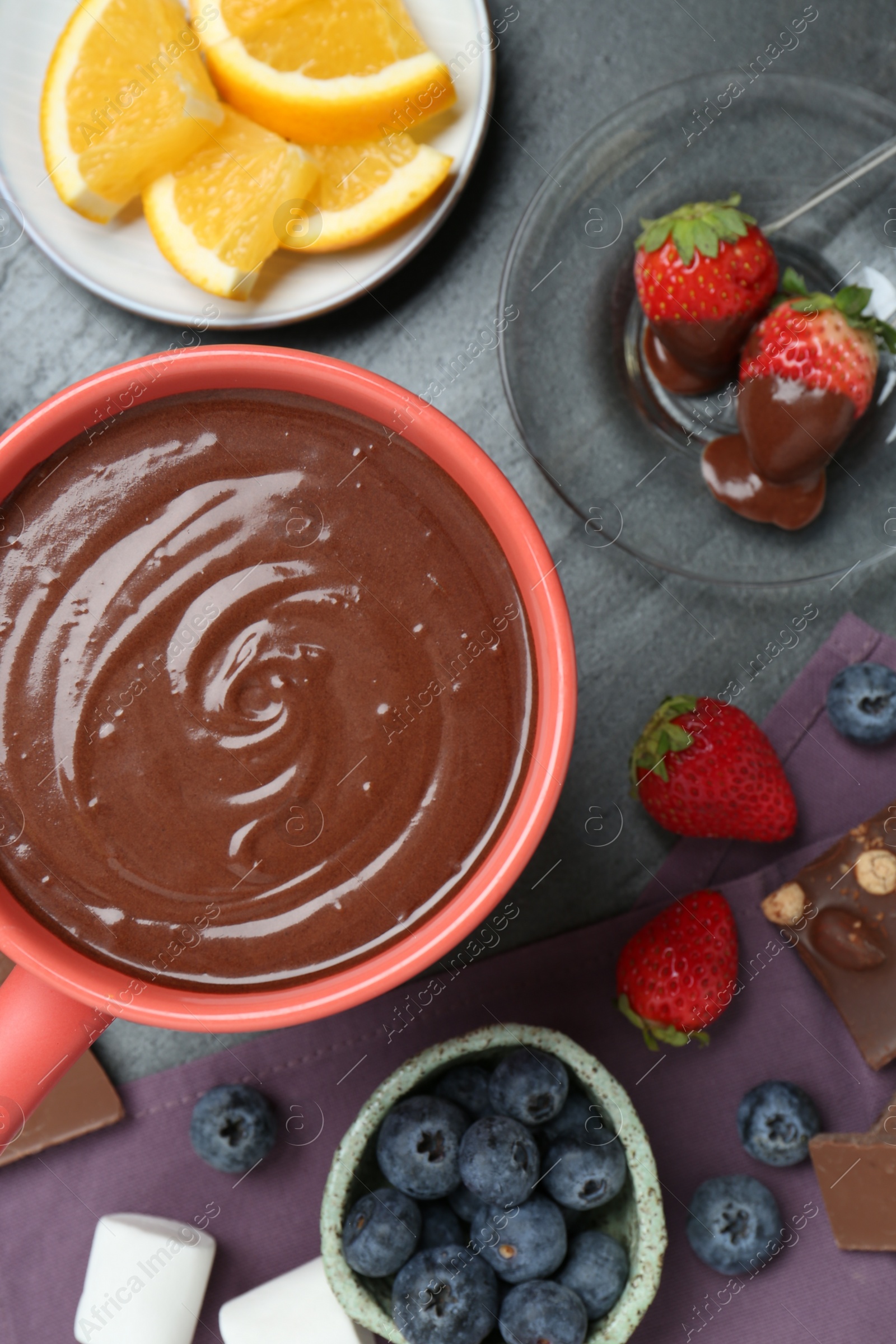 Photo of Fondue pot with melted chocolate, marshmallows, fresh orange and different berries on grey table, flat lay