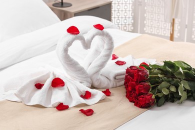 Photo of Honeymoon. Swans made of towels and beautiful red roses on bed in room