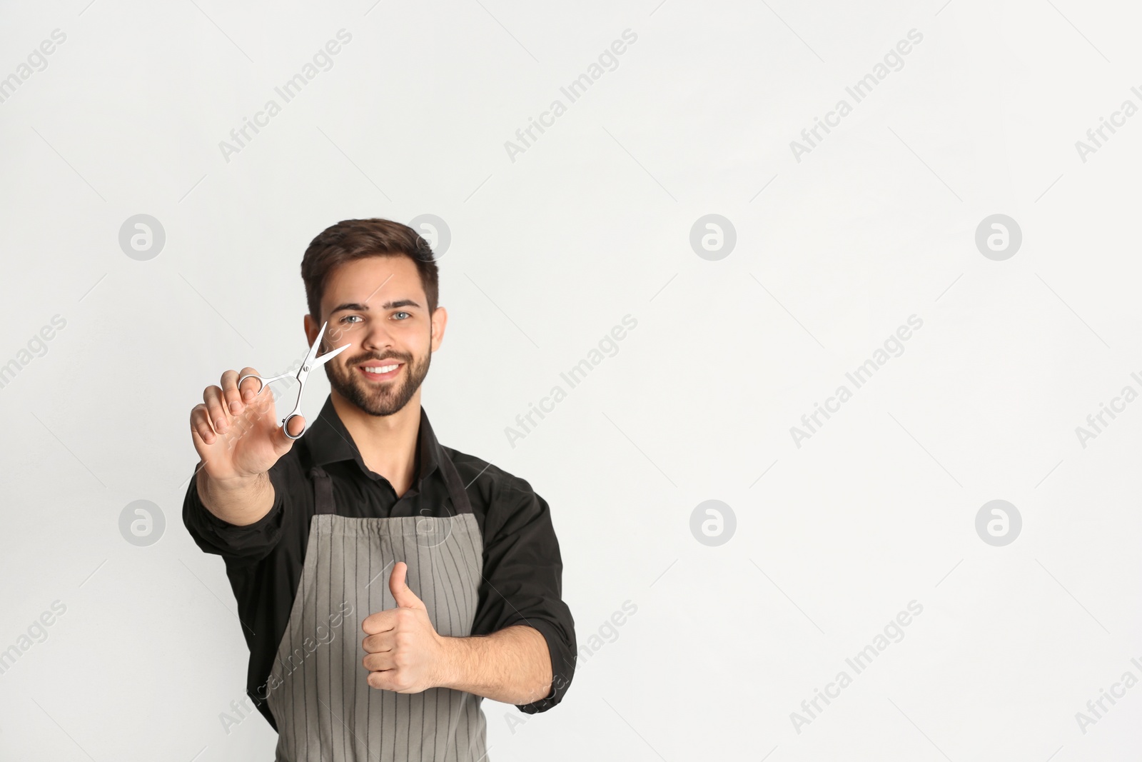 Photo of Young hairstylist holding professional scissors on light background