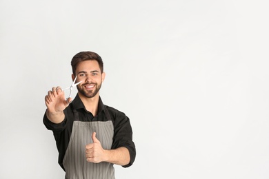 Photo of Young hairstylist holding professional scissors on light background