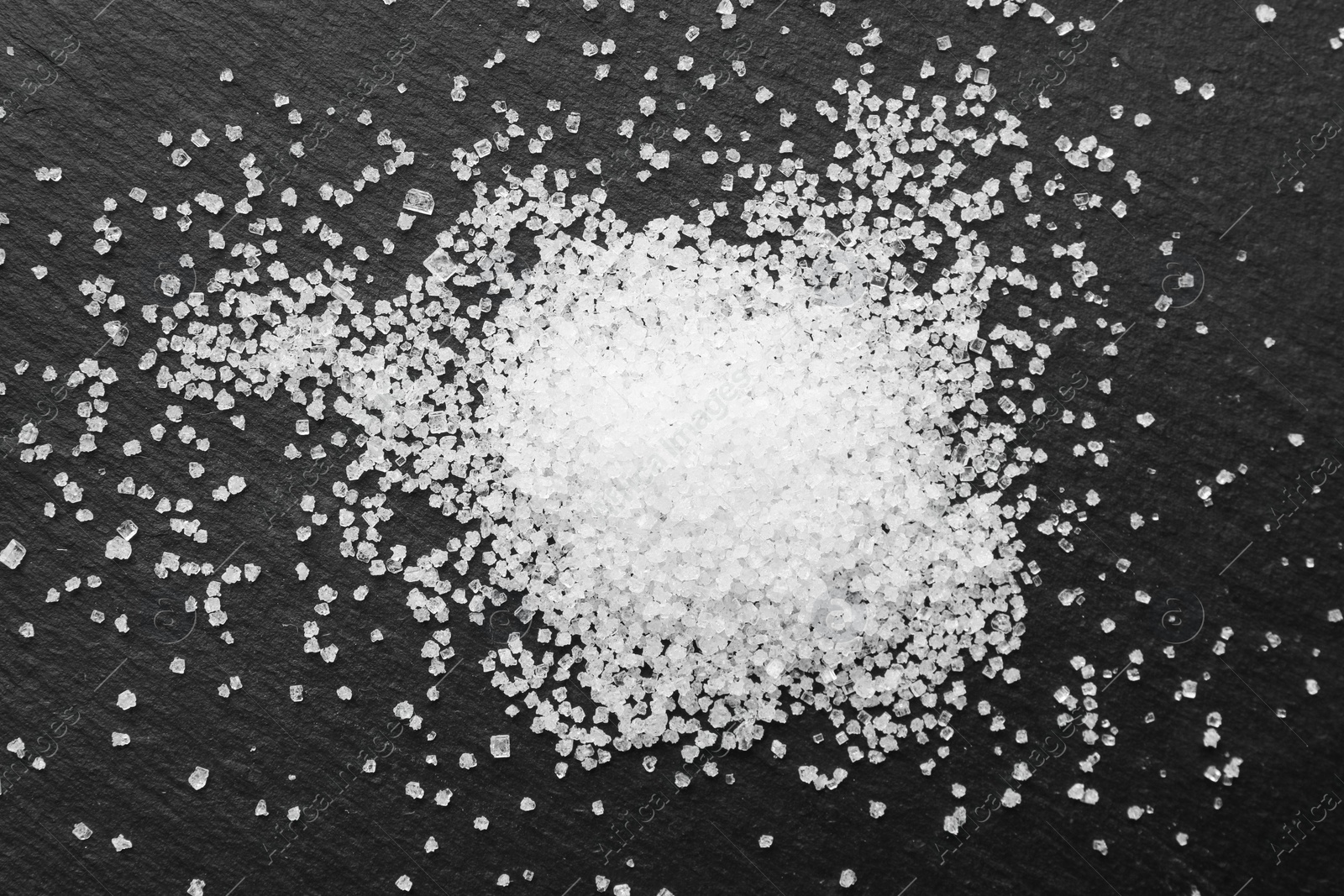 Photo of Heap of granulated sugar on black table, top view