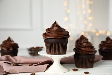 Delicious chocolate cupcakes with cream on white table against blurred lights