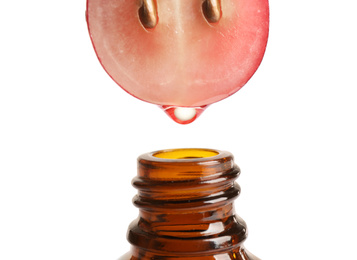 Natural grape seed essential oil dripping from berry into bottle on white background, closeup. Organic cosmetics