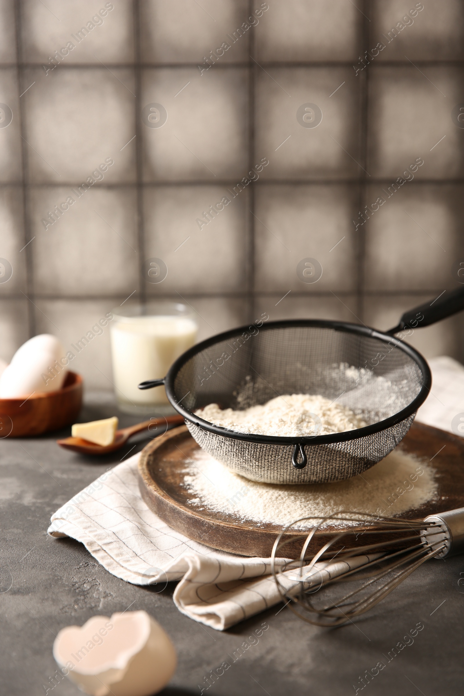 Photo of Flour in sieve and other ingredients for dough on grey textured table. Space for text