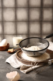 Flour in sieve and other ingredients for dough on grey textured table. Space for text