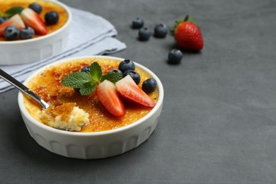 Photo of Delicious creme brulee with berries in bowl and spoon on grey table. Space for text