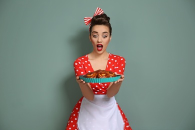 Funny young housewife with homemade pastry on color background