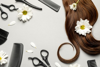Photo of Flat lay composition with professional hairdresser tools, flowers and brown hair strand on light grey background. Space for text