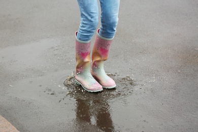 Photo of Woman jumping in rubber boots under rain on street, closeup