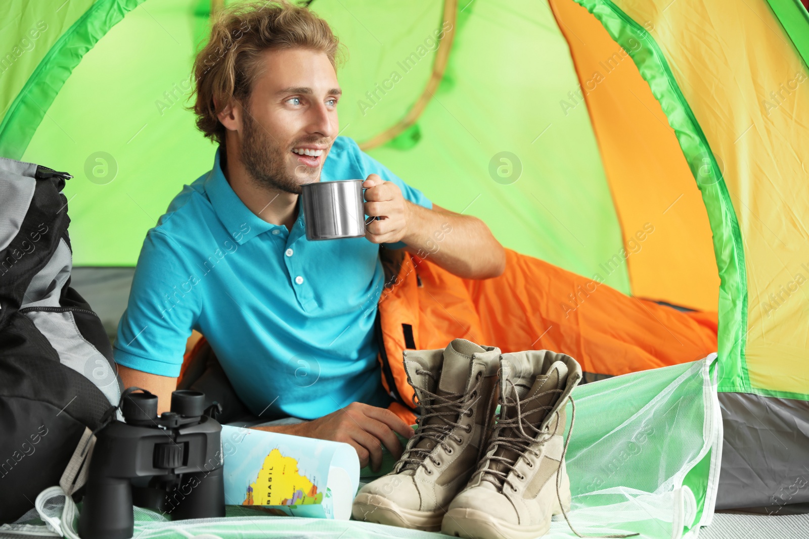 Photo of Young man in sleeping bag with mug inside of tent