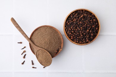 Photo of Aromatic clove powder and dried buds on white tiled table, top view