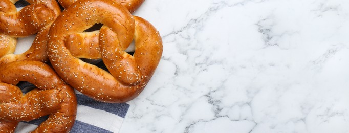 Delicious pretzels with sesame seeds on white marble table, flat lay with space for text. Banner design