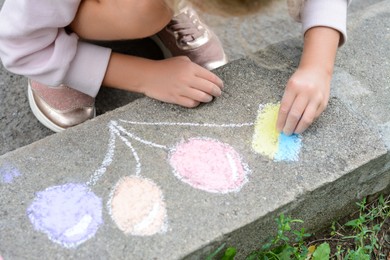 Photo of Little child drawing balloons and ukrainian flag with chalk on curb outdoors, closeup