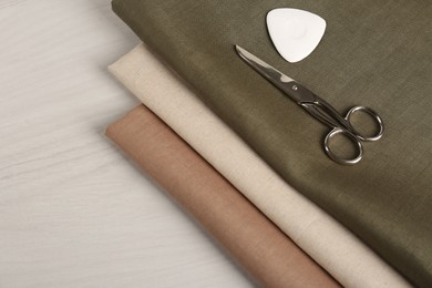 Photo of Different fabrics, scissors and tailor's chalk on light beige wooden table