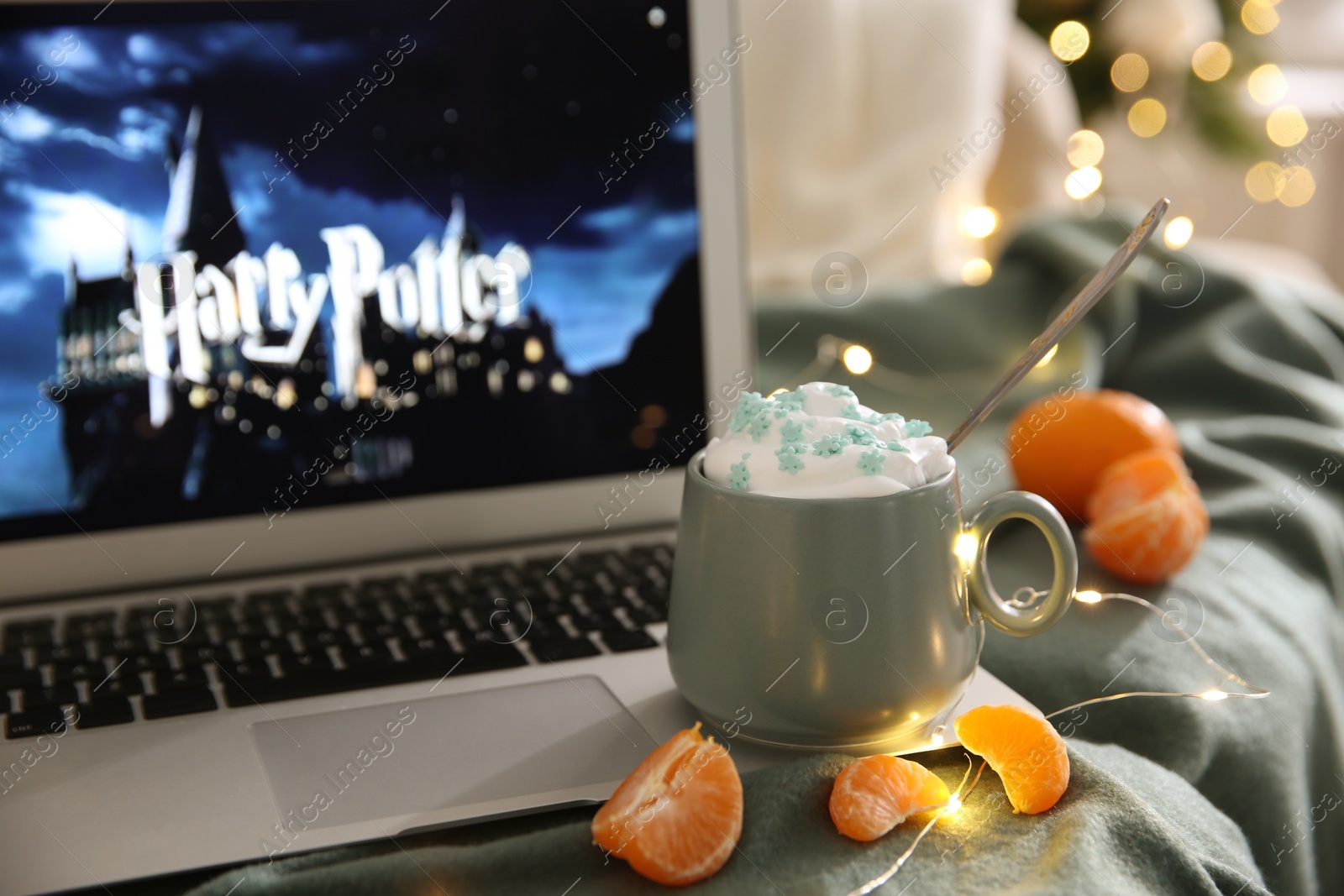 Photo of MYKOLAIV, UKRAINE - DECEMBER 25, 2020: Laptop displaying Harry Potter movie indoors, focus on cup of sweet drink and tangerine slices.  Cozy winter holidays atmosphere