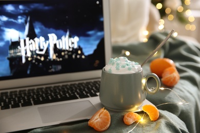 MYKOLAIV, UKRAINE - DECEMBER 25, 2020: Laptop displaying Harry Potter movie indoors, focus on cup of sweet drink and tangerine slices.  Cozy winter holidays atmosphere