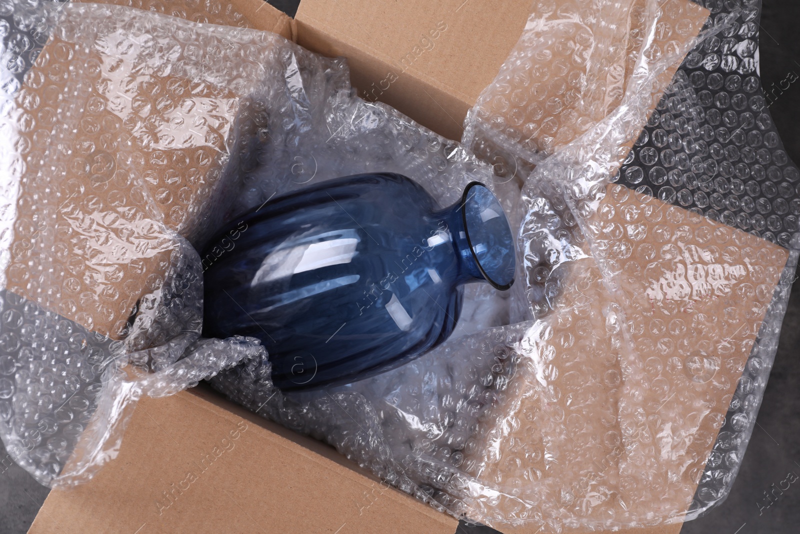 Photo of Beautiful glass vase in box with bubble wrap on dark grey table, top view