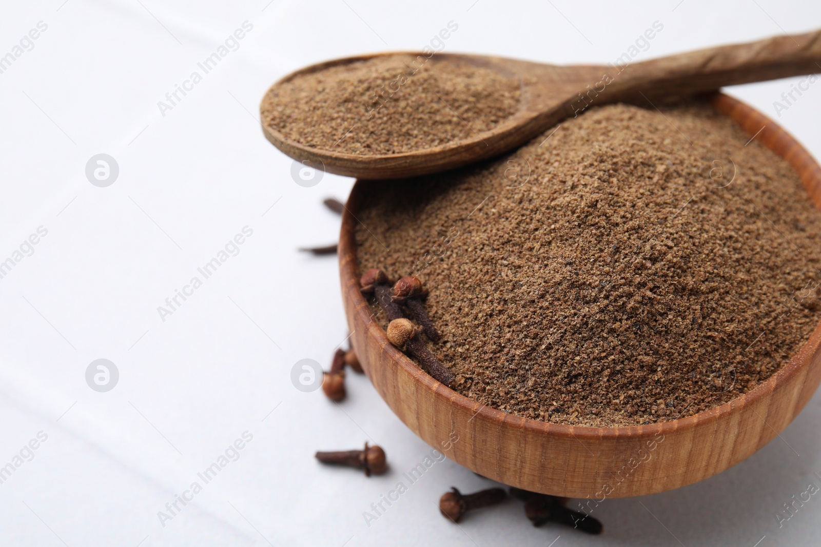 Photo of Aromatic clove powder in bowl, dried buds and spoon on white table, closeup. Space for text