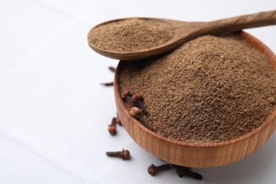 Photo of Aromatic clove powder in bowl, dried buds and spoon on white table, closeup. Space for text