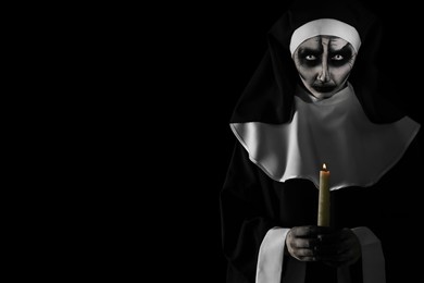 Photo of Scary devilish nun with burning candle on black background, space for text. Halloween party look