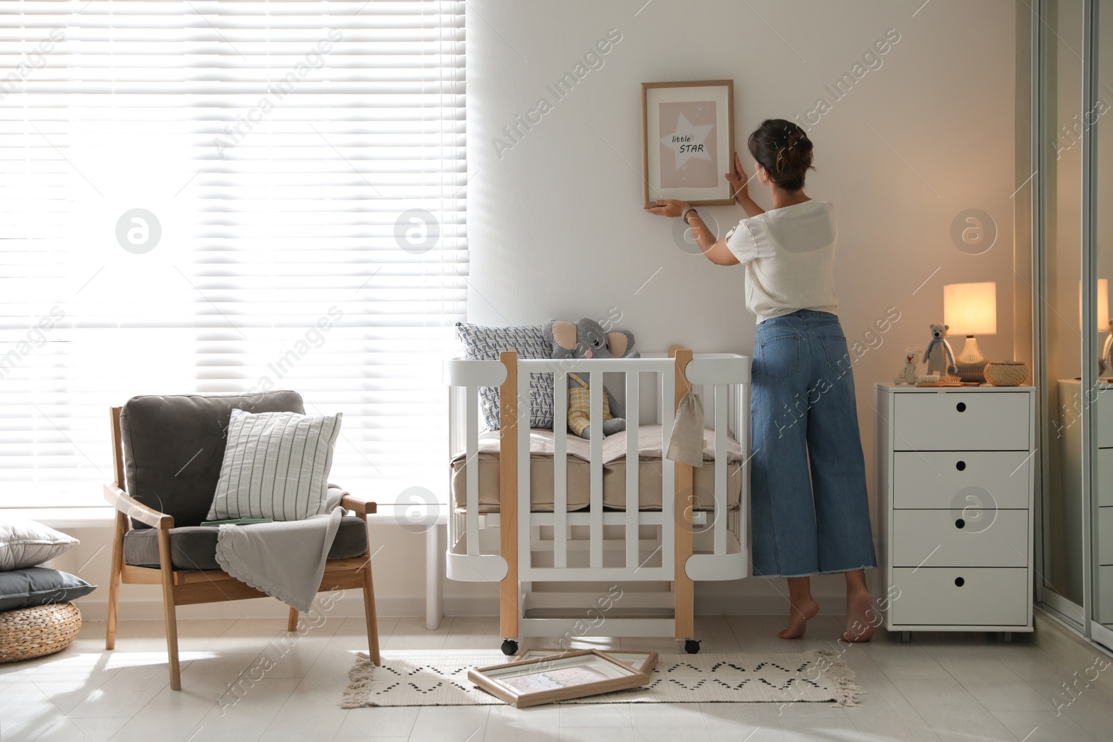 Photo of Decorator hanging picture on wall in baby room. Interior design