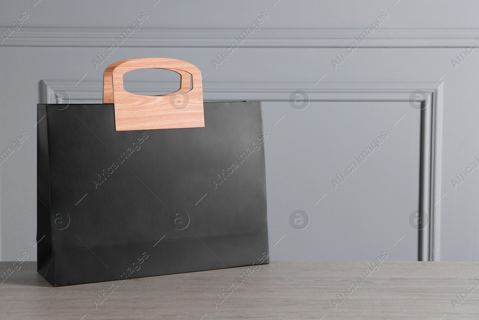 Photo of Black paper bag on wooden table against light grey wall, space for text