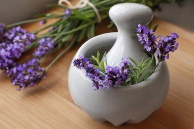 Mortar with fresh lavender flowers, rosemary and pestle on wooden table