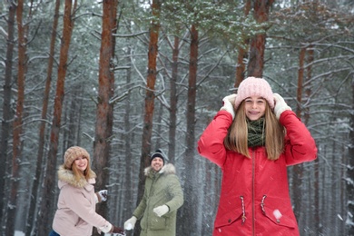 Teenage girl playing snowballs with family in winter forest