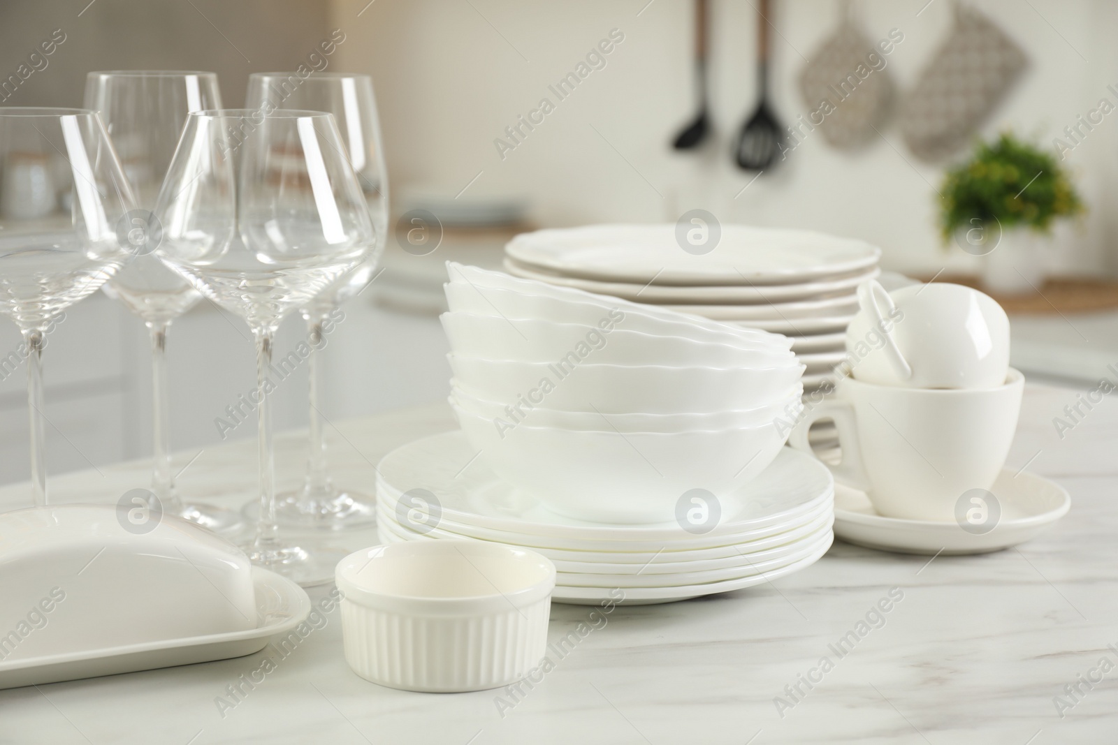 Photo of Clean plates, bowls, cups and glasses on white marble table in kitchen