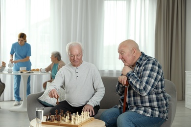 Photo of Elderly men playing chess at nursing home. Assisting senior people