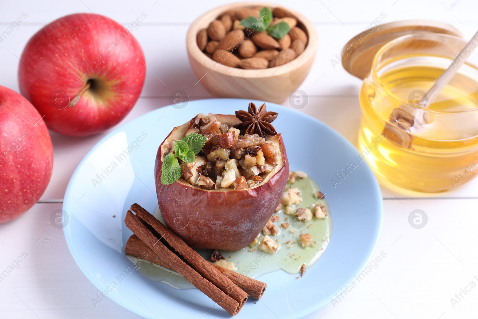 Photo of Tasty baked apple with nuts, honey, spices and mint on white wooden table, closeup