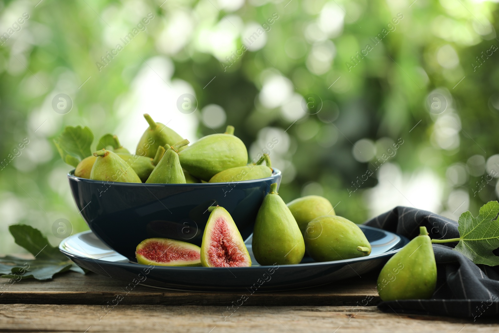 Photo of Cut and whole green figs on wooden table against blurred background, space for text