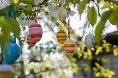 Photo of Beautifully painted Easter eggs hanging on blooming tree outdoors