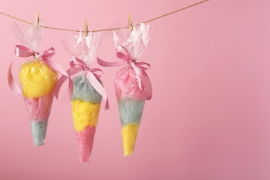 Photo of Packaged sweet cotton candies hanging on clothesline against pink background, space for text