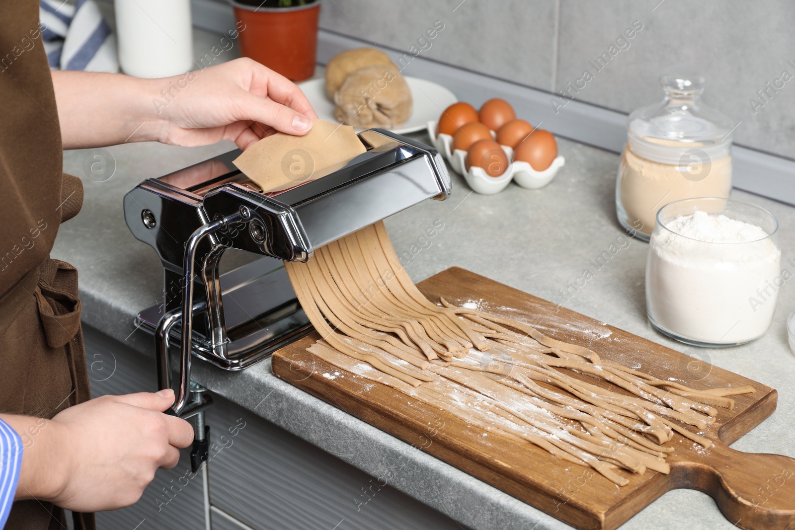 Photo of Woman making soba with pasta machine at table in kitchen, closeup