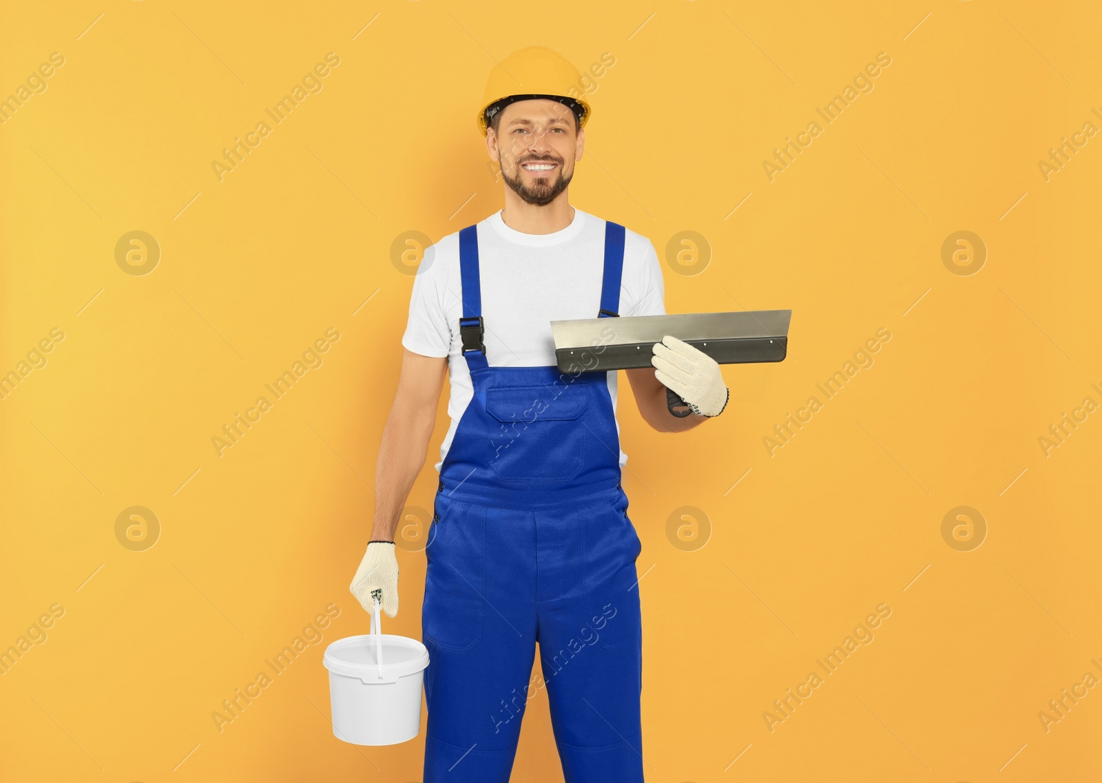 Photo of Professional worker with putty knife and plaster in hard hat on orange background