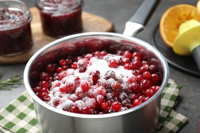 Photo of Making cranberry sauce. Fresh cranberries with sugar in saucepan on table, closeup