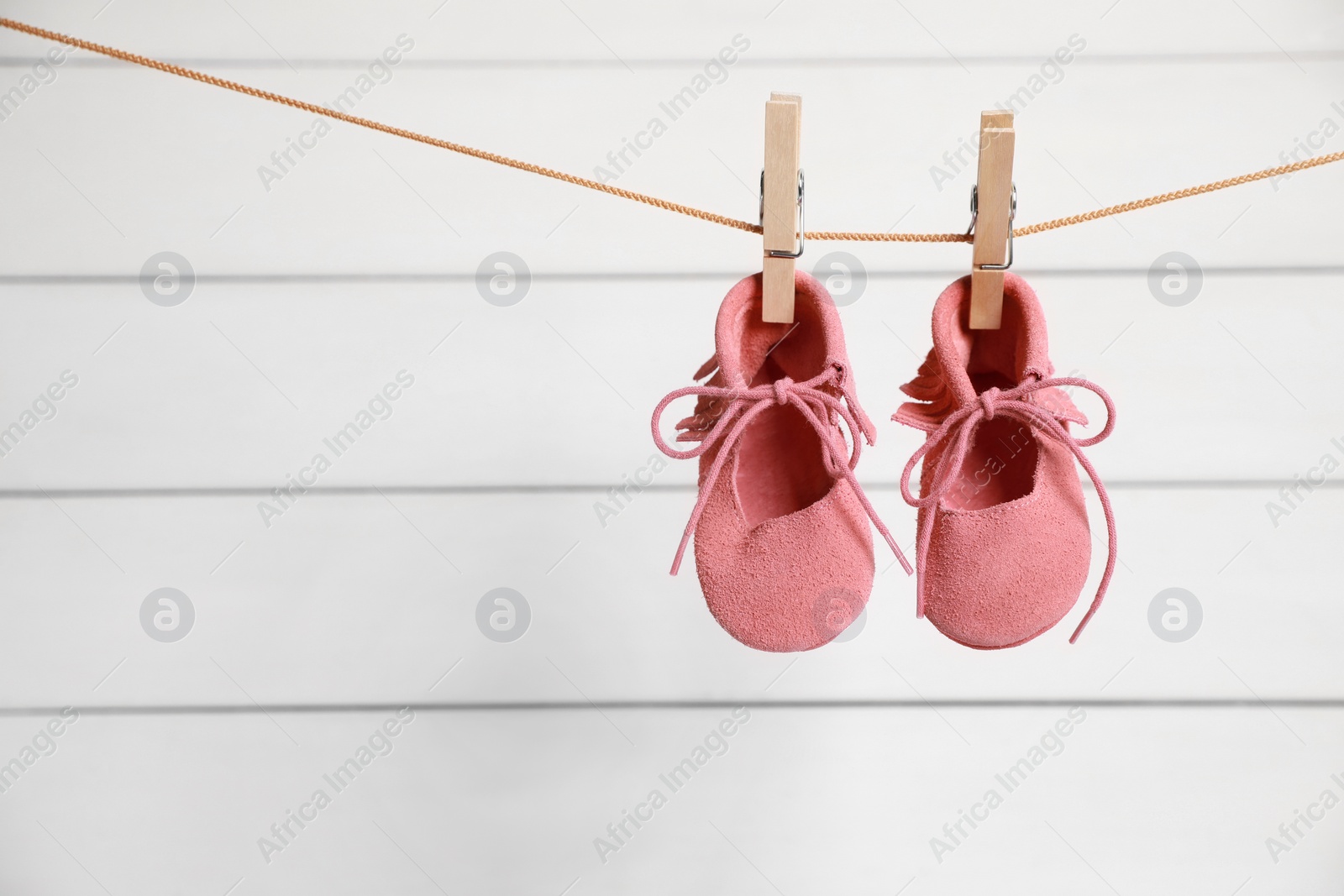 Photo of Pink baby shoes drying on washing line against white wall. Space for text