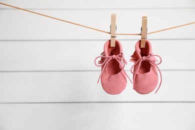 Photo of Pink baby shoes drying on washing line against white wall. Space for text