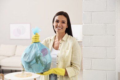 Photo of Woman holding full garbage bag at home