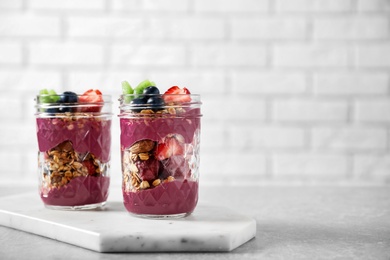 Delicious acai dessert with granola and berries in jars on table against white brick wall. Space for text