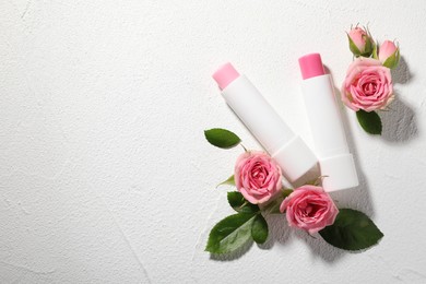 Photo of Lip balms and rose flowers on white textured background, flat lay. Space for text