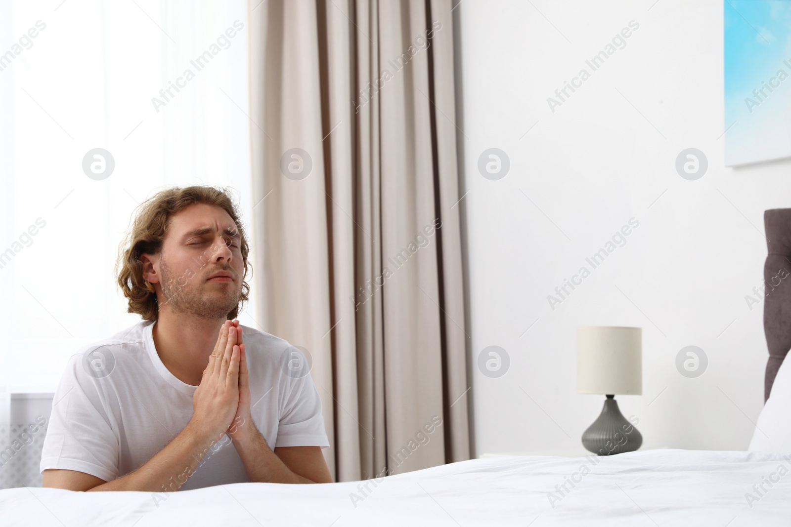 Photo of Handsome young man saying bedtime prayer at home. Space for text