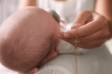 Photo of Mother holding Christian cross near newborn baby indoors, closeup