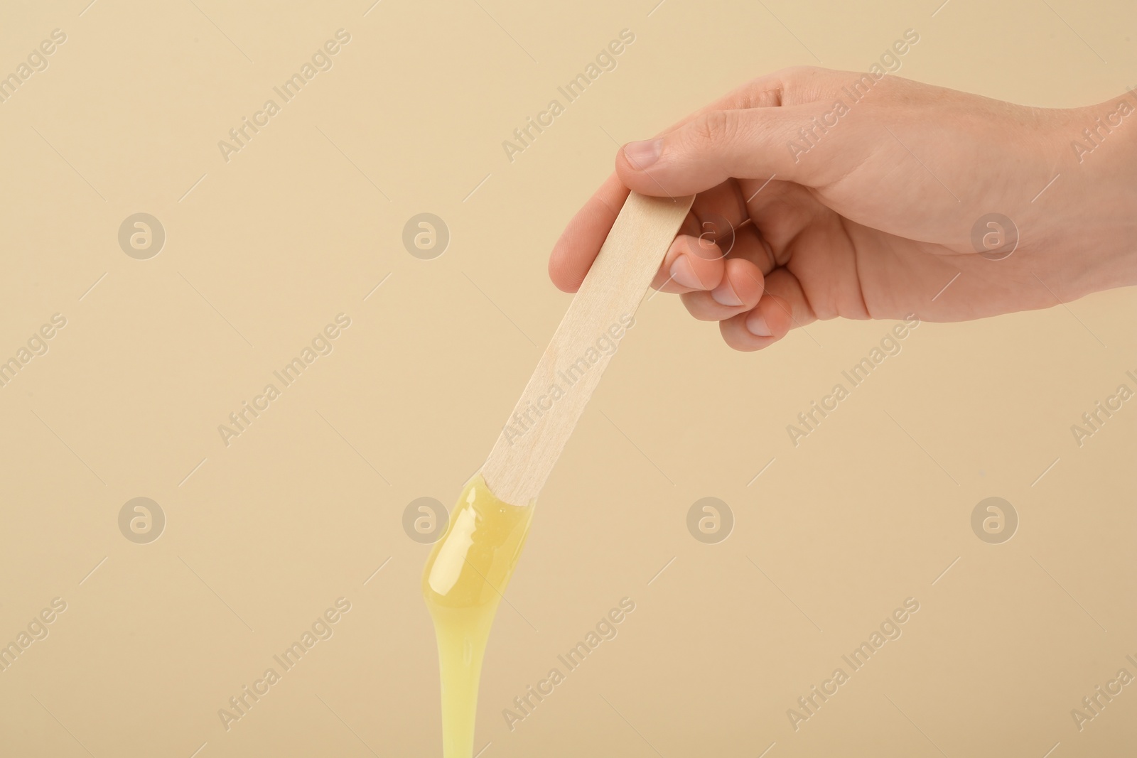 Photo of Woman holding spatula with hot depilatory wax on beige background, closeup