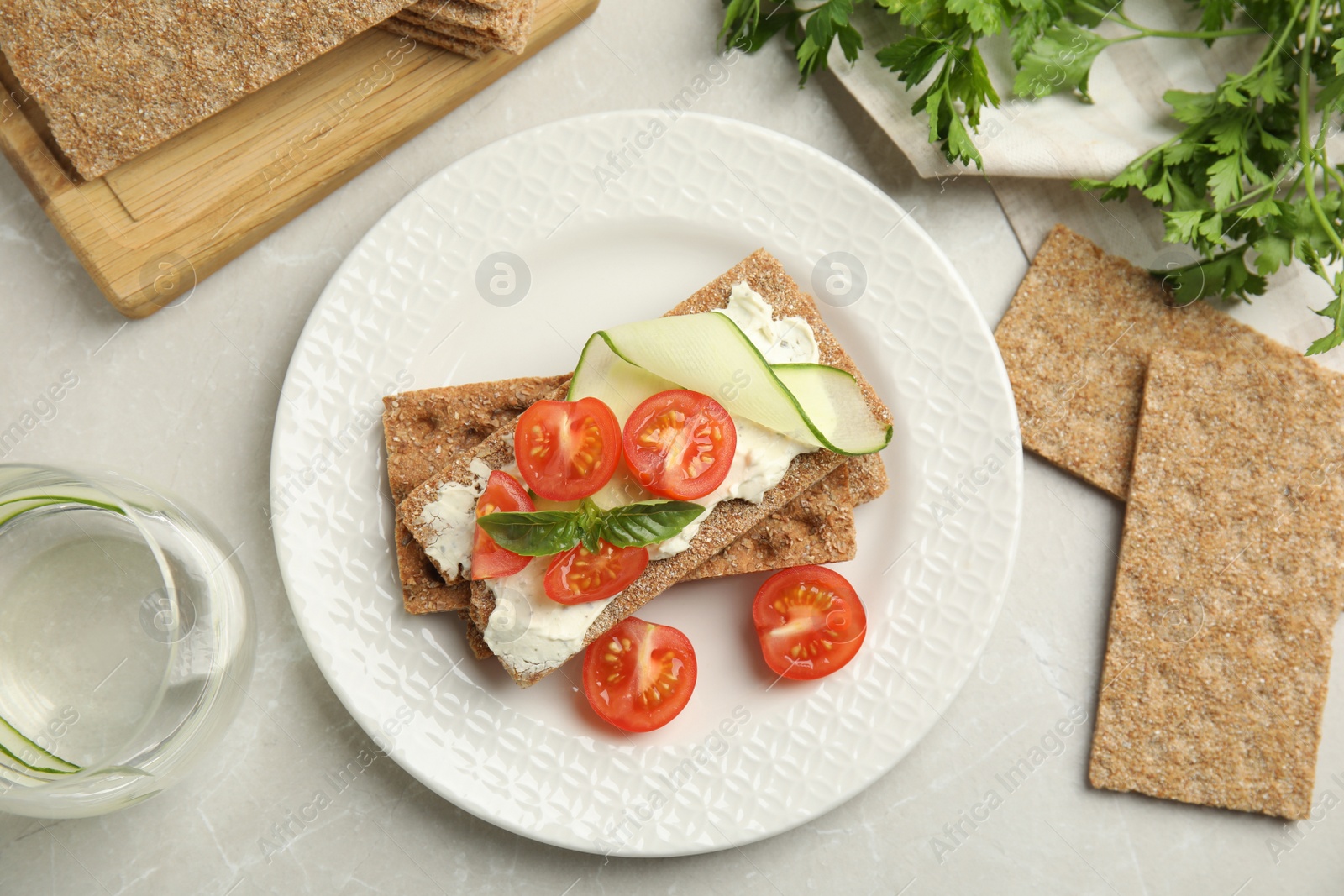 Photo of Fresh rye crispbreads with cream cheese and vegetables on light grey marble table, flat lay